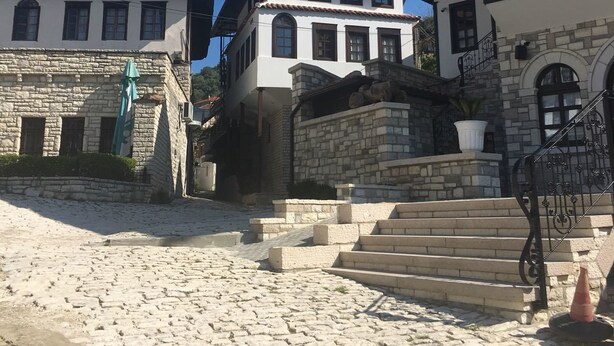 A cobblestone courtyard with stone buildings, a staircase, and a clear blue sky. - Guesthouse Altin (Berat)