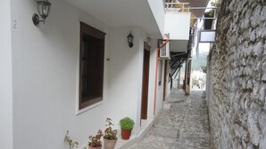 A narrow cobblestone street flanked by white buildings with potted plants and a stone wall. - Guesthouse Altin (Berat)