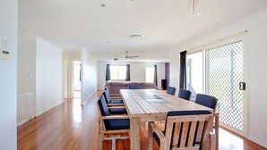 A spacious living area with a long wooden table, multiple chairs, a sofa, and a large window with a view. - 29 Cypress Avenue - Rainbow Beach. Close to the beach with a pool (RAINBOW BEACH)