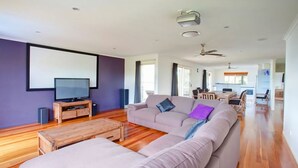 A spacious living room with a large flat-screen TV, a wooden coffee table, and a beige sectional sofa. - 29 Cypress Avenue - Rainbow Beach. Close to the beach with a pool (RAINBOW BEACH)