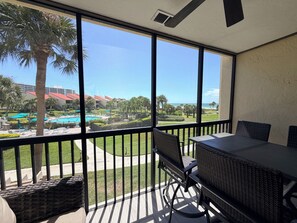 Un balcón con vista a una piscina, palmeras y un edificio con techos rojos.