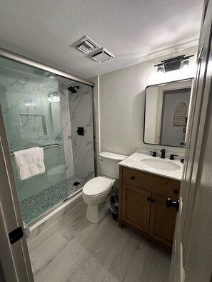 Un baño moderno con cabina de ducha de vidrio, inodoro, lavabo con espejo y muebles de madera.