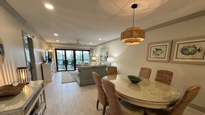 A modern dining area with a round glass table, wicker chairs, and a hanging light fixture. - Updated Gulf View Condo in Beautiful Siesta Dunes, 5-205 (Siesta Key)