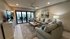 A spacious living room with a grey sofa set, a coffee table, a TV, and a painting on the wall. - Updated Gulf View Condo in Beautiful Siesta Dunes, 5-205 (Siesta Key)