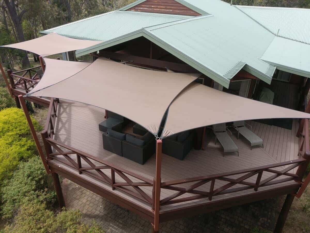 A covered outdoor seating area with a wooden deck and metal roof, surrounded by greenery.