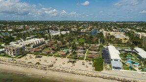 Vista aérea de un complejo turístico costero con varios edificios, una playa y un puerto deportivo.