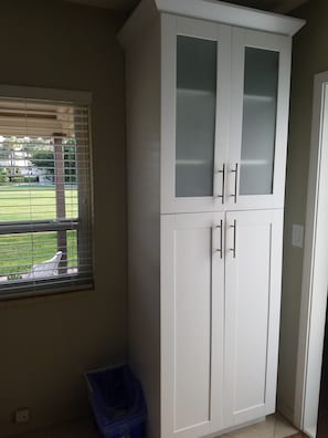 A white cabinet with two doors and a window with blinds.