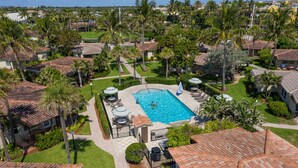 Vista aérea de una zona residencial con piscina rodeada de casas, palmeras y cielo despejado.