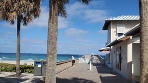 Un paseo marítimo con palmeras, vistas a la playa y un edificio con un letrero que dice 'SHOP'.