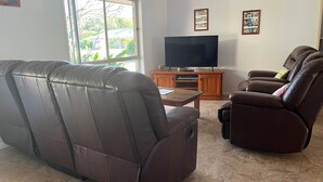 A living room with a leather sofa, a recliner, a coffee table, and a flat-screen TV on a wooden stand. - Baker - Rainbow Beach. Walk to Everything! Including the beach and main street. (Rainbow Beach)