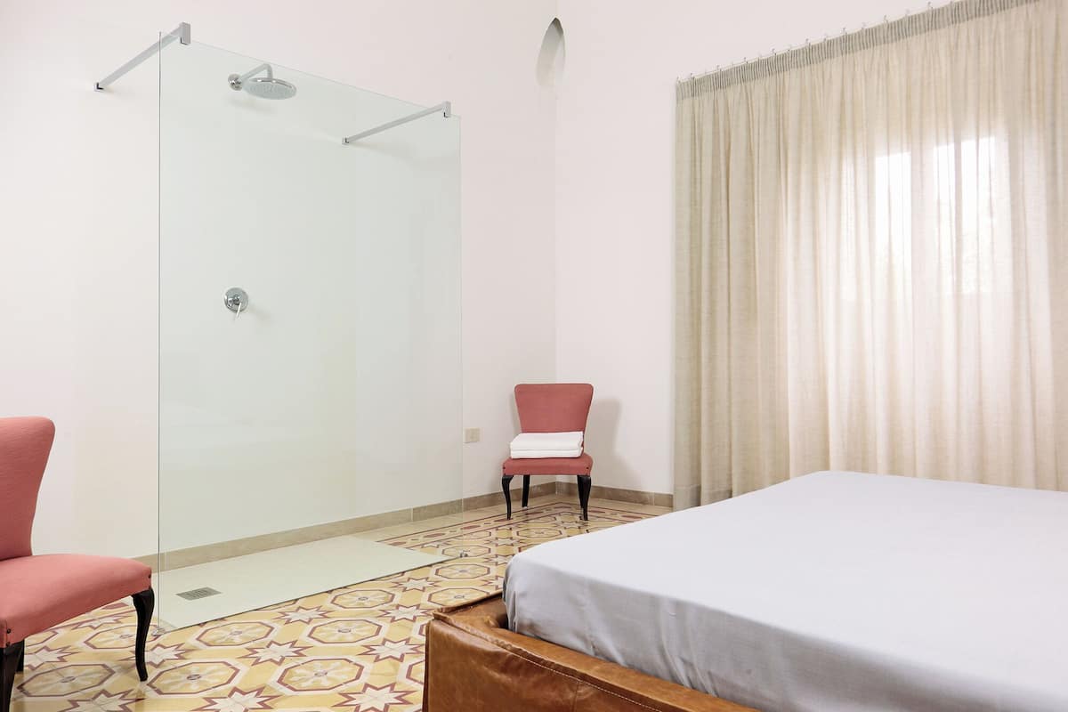 A hotel room with a bed, a chair, a shower, and a patterned floor.