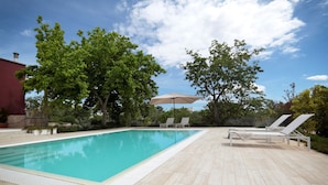 A rectangular swimming pool with a tiled deck, surrounded by trees and a red building. - Villa Aurelia (Castellana Grotte)