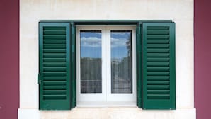 A window with green shutters and a white door, set in a building with a plain facade. - Villa Aurelia (Castellana Grotte)