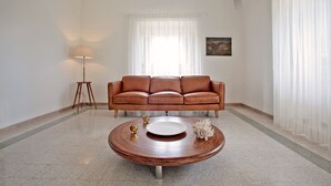 A living room with a brown leather sofa, a round wooden coffee table with decorative items, a floor lamp, and a painting on the wall. - Villa Aurelia (Castellana Grotte)