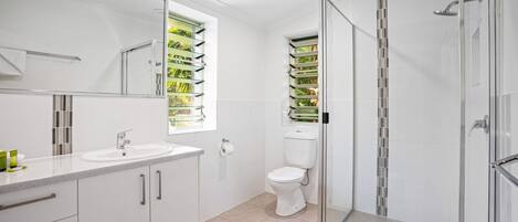 Een moderne badkamer met een douchecabine van glas, een toilet en een wastafel met spiegel erboven.