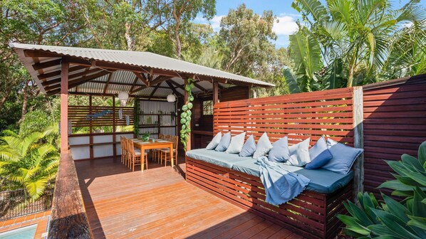 Relax in a serene outdoor space surrounded by lush greenery and trees, featuring a covered patio and comfortable seating.