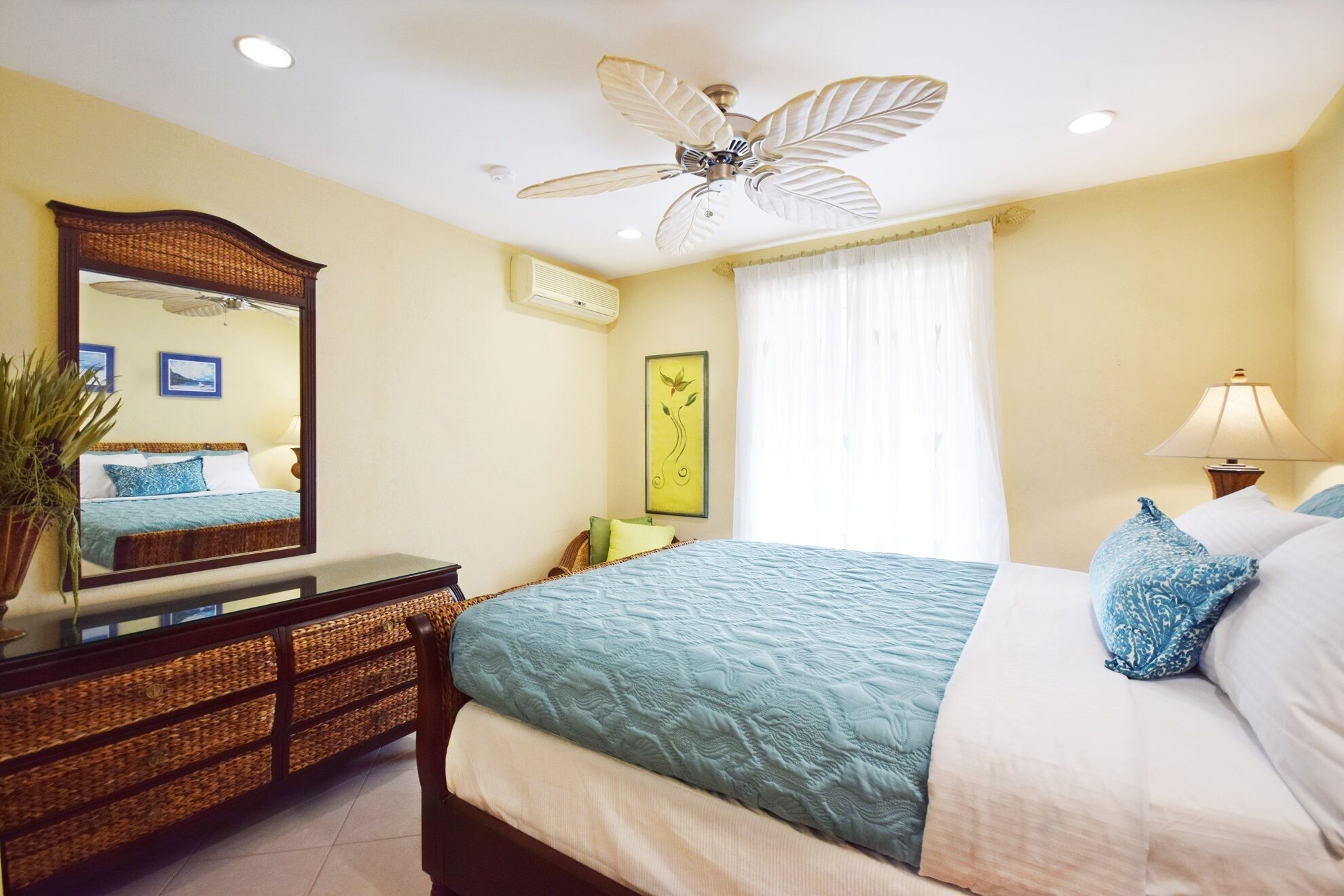 A bedroom with a bed, a dresser, a mirror, a ceiling fan, a window with curtains, and a wall-mounted air conditioner.