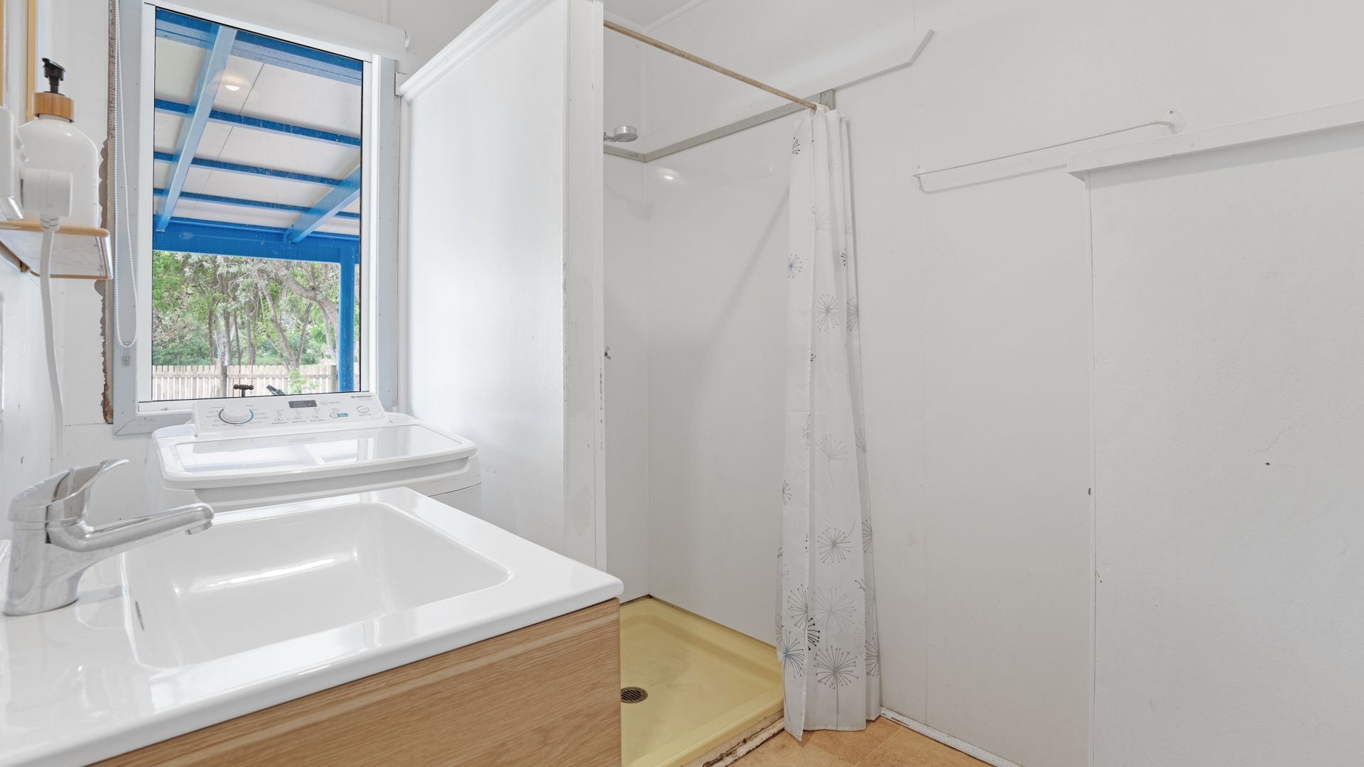 Un baño con lavamanos blanco, ducha y ventana con marco azul.