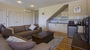A modern living room with a sofa, coffee table, and a kitchen area with cabinets and appliances. - Craiglee (Lorne)