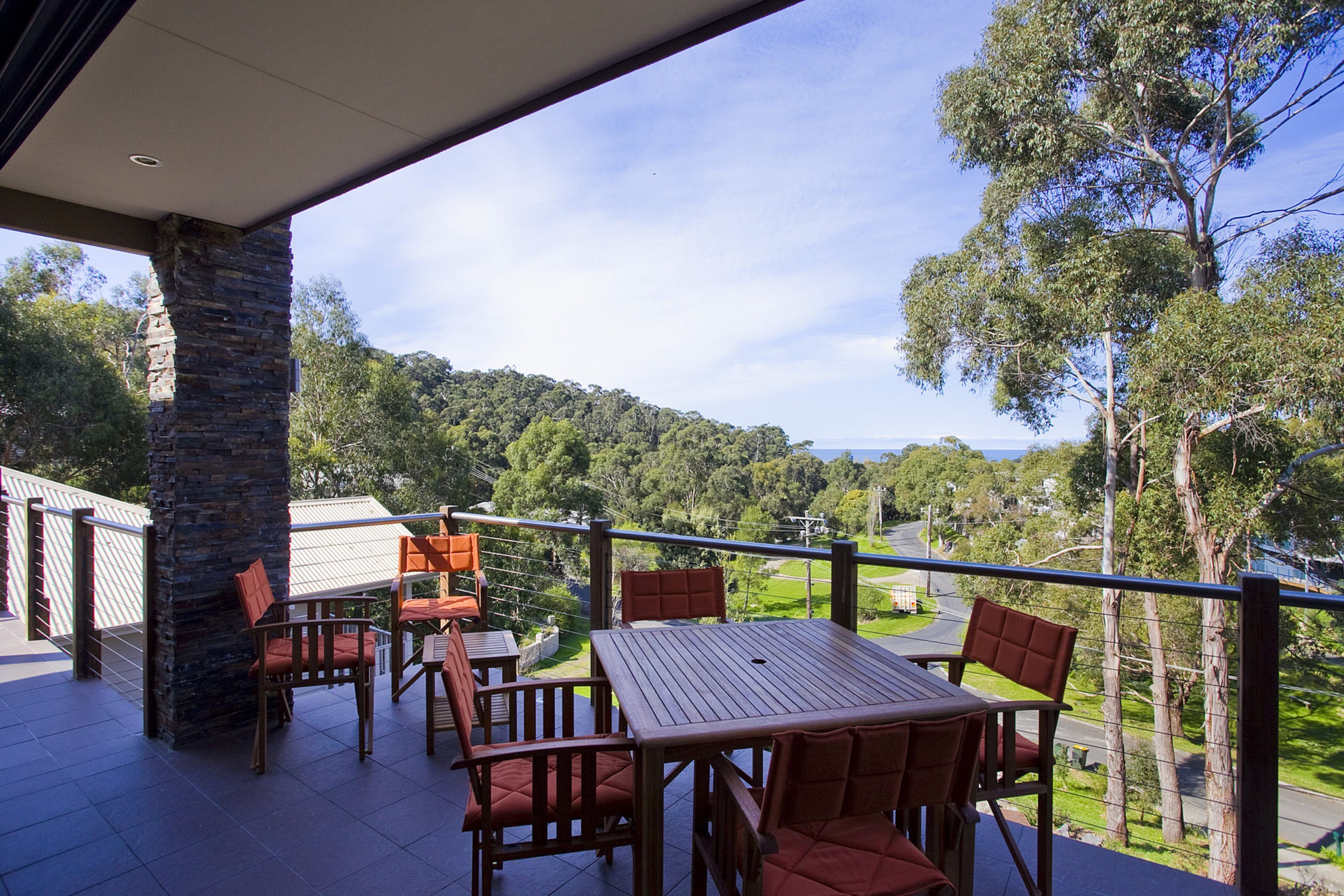 A covered outdoor seating area with a table and chairs, overlooking a hilly landscape with trees.