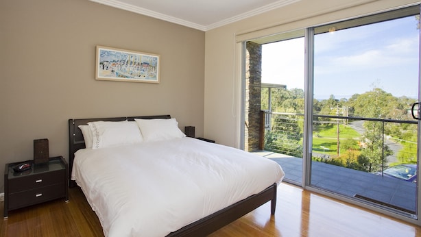 A bedroom with a large bed, a nightstand, a painting on the wall, and a balcony with a view. - Craiglee (Lorne)