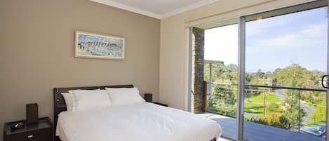 A bedroom with a large bed, a nightstand, a painting on the wall, and a balcony with a view.