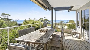 Une terrasse en bois avec une table et des chaises, donnant sur une étendue d’eau.