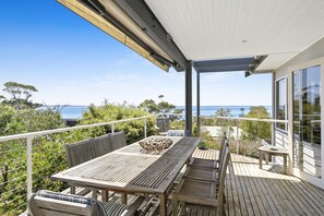 A wooden deck with a table and chairs, overlooking a body of water. - Fernview (Lorne)