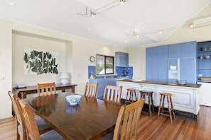 A modern kitchen with blue cabinets, a wooden dining table, and a large island with stools. - Fernview (Lorne)