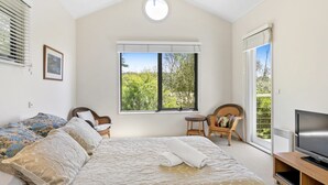 A bedroom with a bed, a chair, a television, and a window with a view of trees. - Fernview (Lorne)
