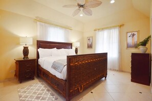 A bedroom with a wooden bed, two bedside tables, a floor lamp, a decorative rug, a ceiling fan, and a painting on the wall. - 3 Min Walk to Beach - Blessed Manor (4 Bed House) (Hastings)