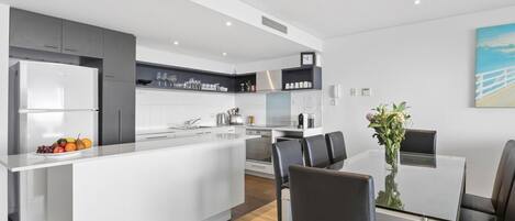 A modern kitchen with a central island, white cabinetry, and a dining area with a glass table and black chairs.