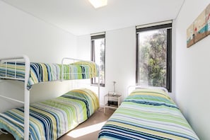 A room with bunk beds, a small bedside table, and a window with a view of trees.