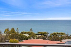 A coastal view with a clear sky, a body of water, and a red-roofed building in the foreground.