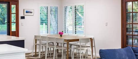 A dining area with a wooden table and white chairs, a blue sofa, and a view through the window blinds.