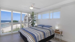 Ein Schlafzimmer mit einem Bett, einem Nachttisch, einer Lampe und einem großen Fenster mit Jalousien.