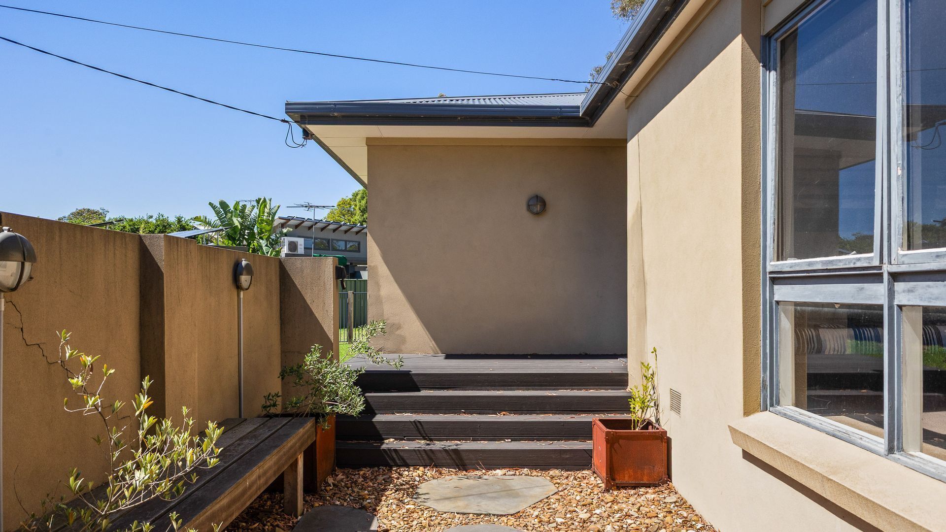 A modern house with a concrete exterior, a large window, and a small garden area with steps leading to the entrance.