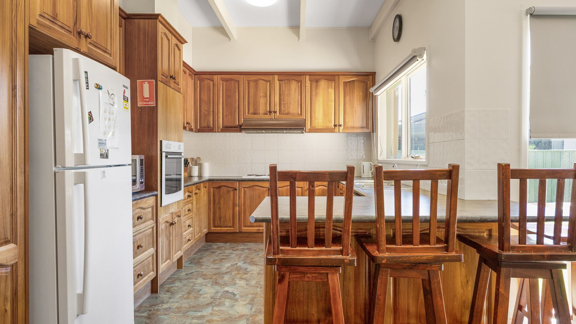 Une cuisine avec des meubles de rangement en bois, un réfrigérateur, un four et une table à manger avec des chaises.