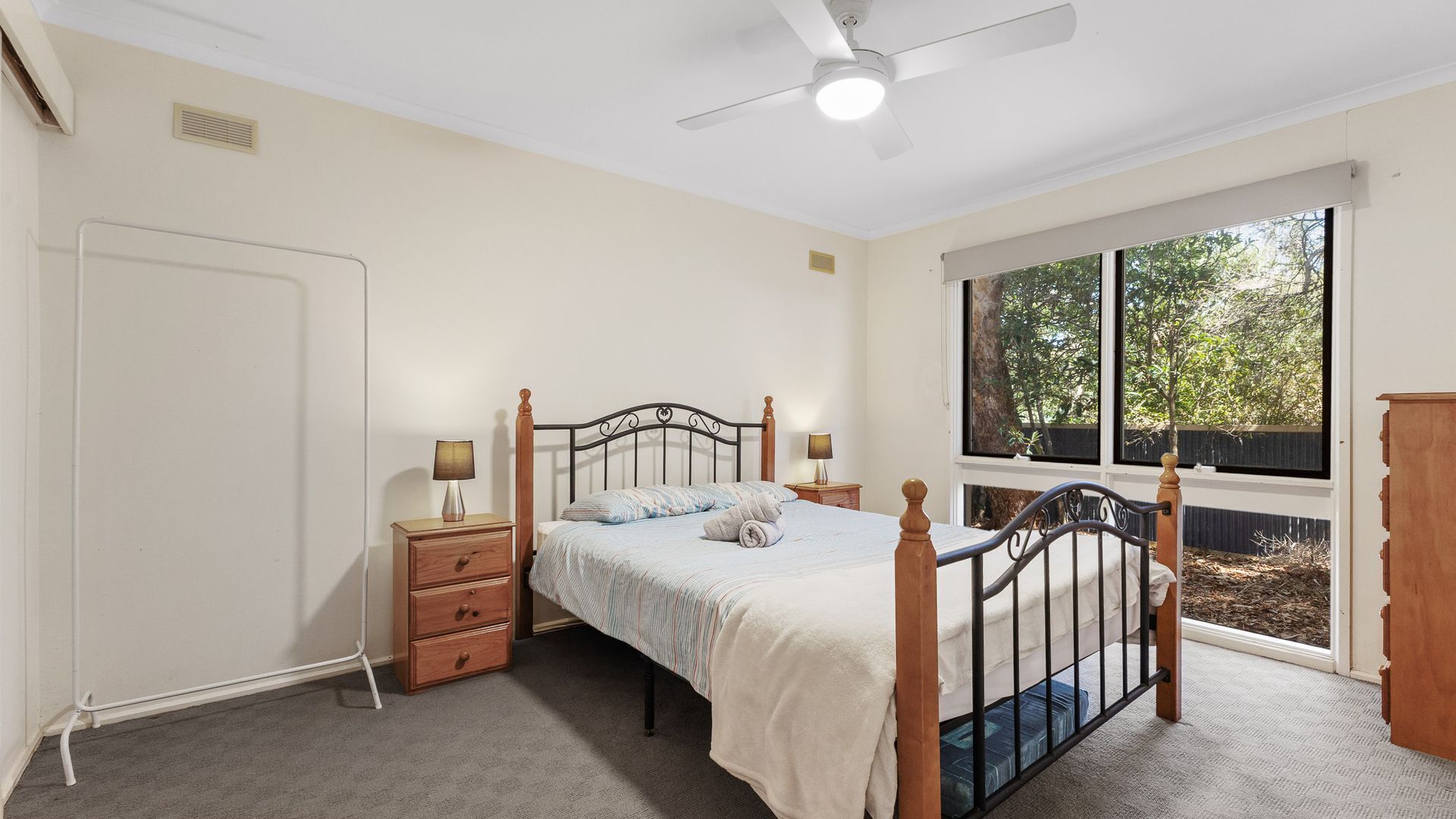 Une chambre à coucher avec un lit, des tables de chevet, un ventilateur de plafond, une fenêtre et une vue sur les arbres.