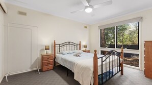 Quarto com cama, mesas de cabeceira, ventoinha no teto, janela e vista para árvores.