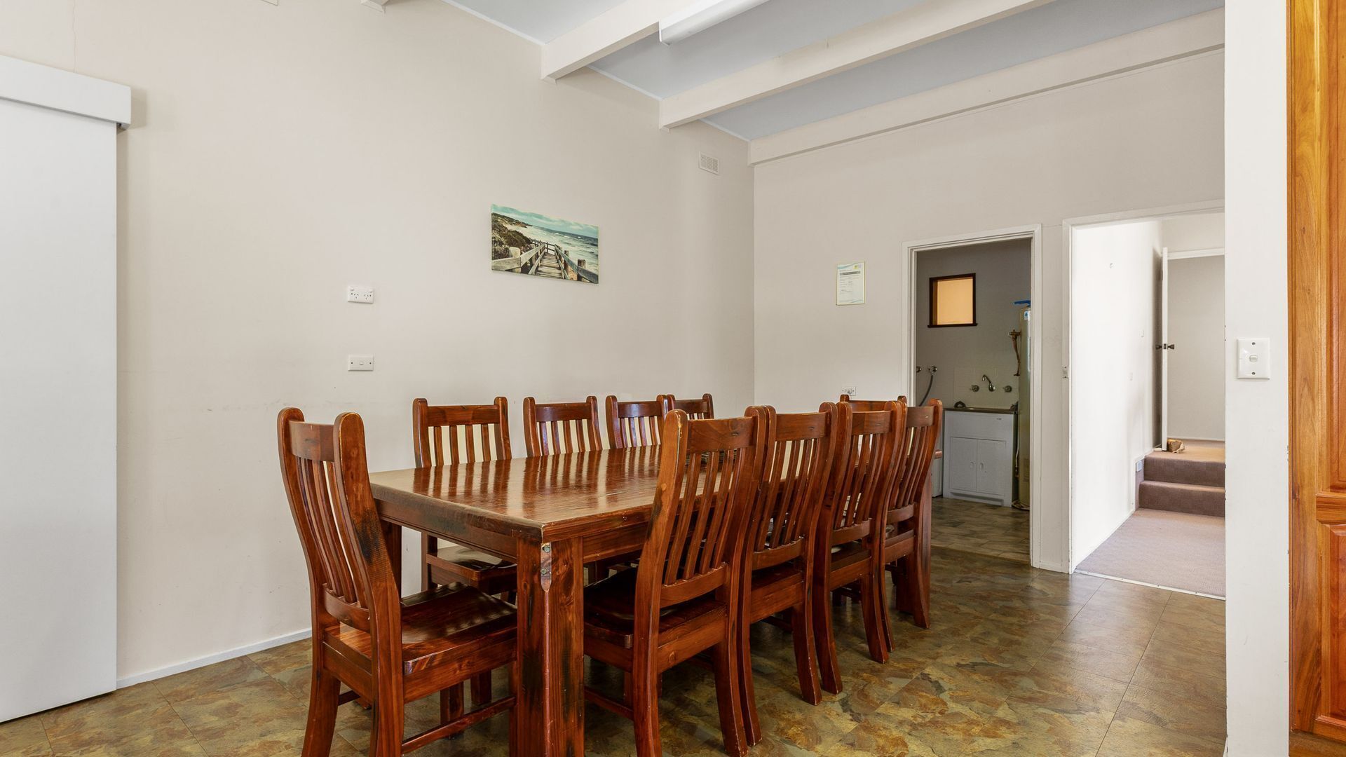 Un coin repas avec une table et des chaises en bois, une cuisine à l’arrière-plan et un petit tableau accroché au mur.