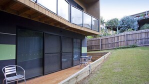 Uma casa moderna com uma grande porta de vidro deslizante, um deck de madeira e um quintal cercado.