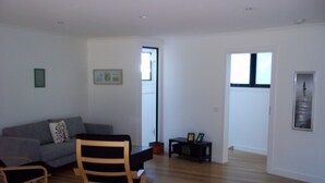 Uma sala de estar ampla com um sofá cinzento, uma cadeira de balanço de madeira e uma mesinha com dois quadros.