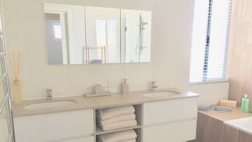 A modern bathroom with a large mirror, two sinks, a shower, and a wooden floor.