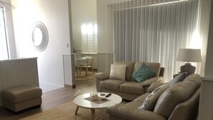 Una sala de estar con un sofá color beige, una mesa de centro y un comedor al fondo.