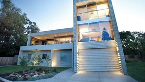 Una casa moderna de dos plantas con techo plano, ventanas amplias e iluminación exterior.