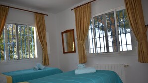 Ein Zimmer mit zwei Betten, jeweils mit blauer Bettdecke und gelben Akzenten. Es gibt Fenster mit Vorh ängen, einen Spiegel an der Wand und eine Heizung.