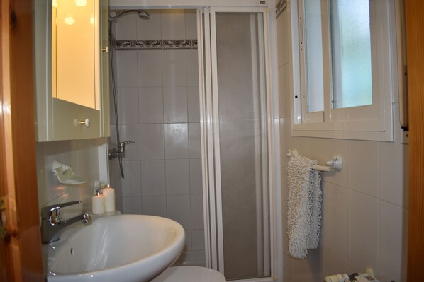 A bathroom with a sink, toilet, shower, and a towel hanging on the wall.