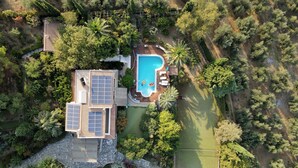 An aerial view of a house with a swimming pool, solar panels, and a tennis court.