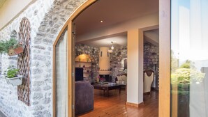 A stone-walled room with a fireplace, wooden flooring, and a glass door leading outside.